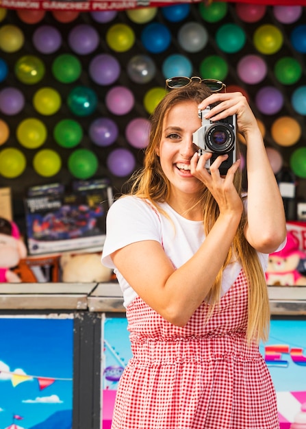 Foto grátis mulher nova de sorriso que toma retratos com a câmera no parque de diversões