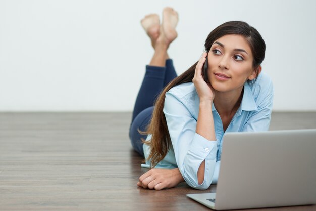 Mulher nova que convida o telefone e deitado no chão