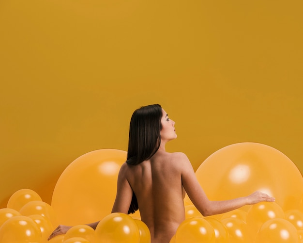 Mulher nua entre muitos balões amarelos