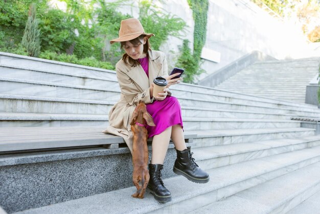 Mulher ocupada smartphone e filhote de dachshund ao ar livre