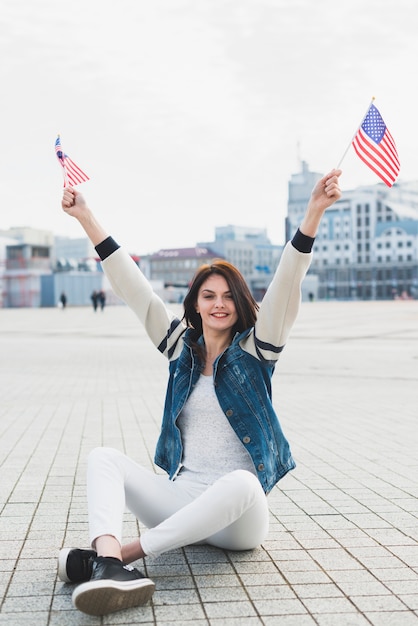 Mulher olha, câmera, sentando, ligado, quadrado, e, waving, bandeiras americanas, em, mãos