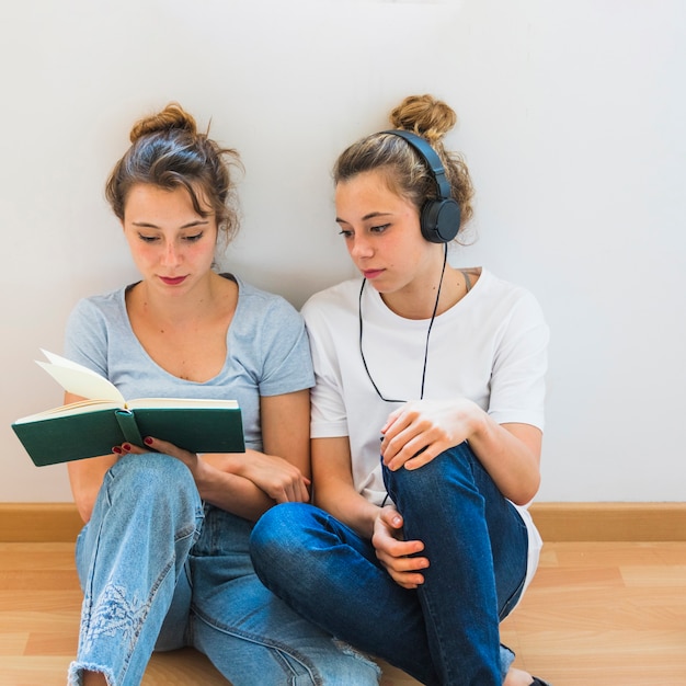 Foto grátis mulher olha, em, dela, irmã, livro leitura, sentar chão hardwood