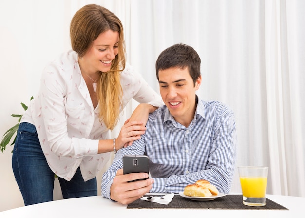 Foto grátis mulher olhando homem tomando café da manhã usando o telefone móvel