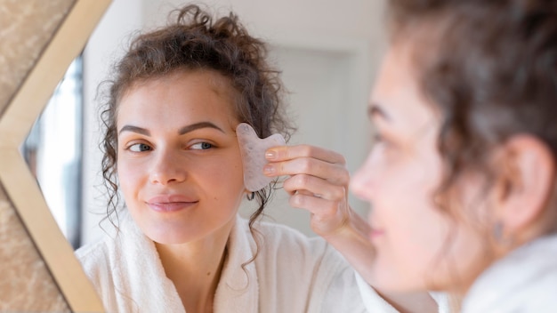 Mulher olhando no espelho e fazendo massagem facial