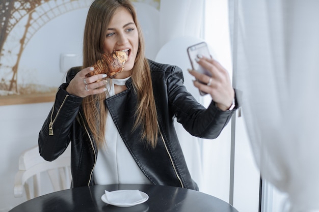 Foto grátis mulher olhando para seu celular enquanto se come um croissant