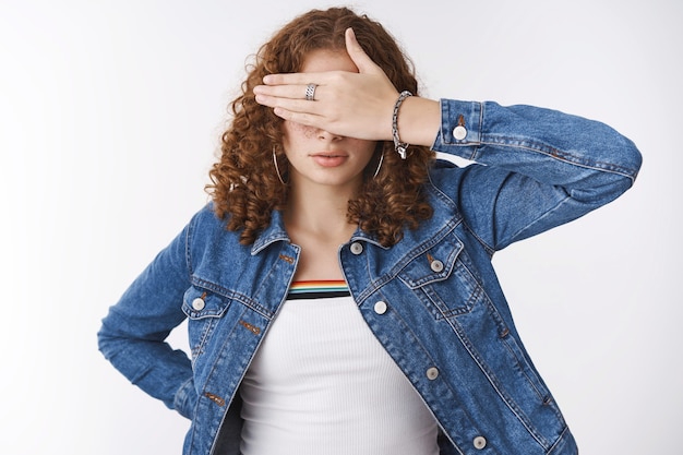 Mulher olhos fechados realizando pose de cegueira esconder a visão com a palma da mão olhar sério sem vontade de ver, prometa não espiar. esperando o comando, em pé, fundo branco e jaqueta jeans