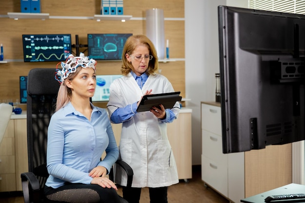 Mulher paciente escaneando seu cérebro e médico fazendo anotações no tablet segurando-o na mão. Dispositivo de varredura de ondas cerebrais