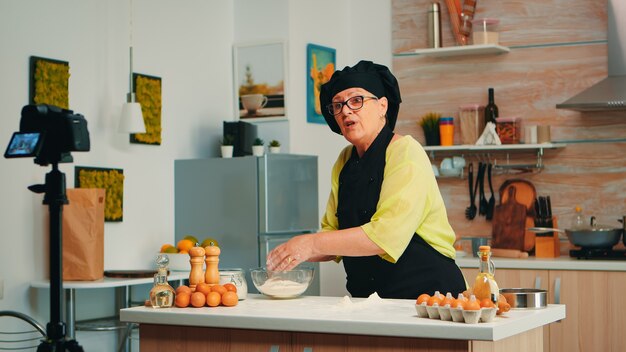 Mulher padeiro apresentando receita durante a gravação de tutorial para mídia social. Influenciador chef de blogueiro aposentado que usa tecnologia da Internet para se comunicar, filmar, fazer um blog em podcast com equipamento digital