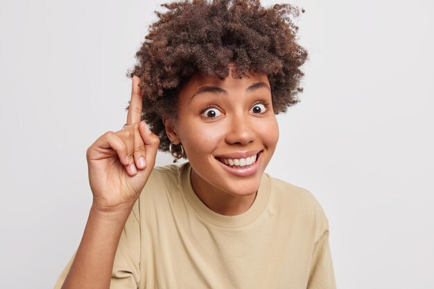 mulher parece surpreendentemente sorrindo feliz indica dedo indicador acima vestido casualmente isolado no branco dá informações