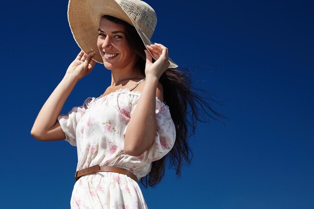 Mulher pega chapéu de verão soprado pelo vento usa vestido floral
