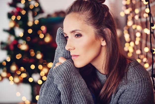 Mulher pensando em casa com luzes de Natal na parede