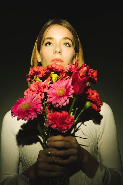 Mulher pensativa com buquê de flores brilhantes