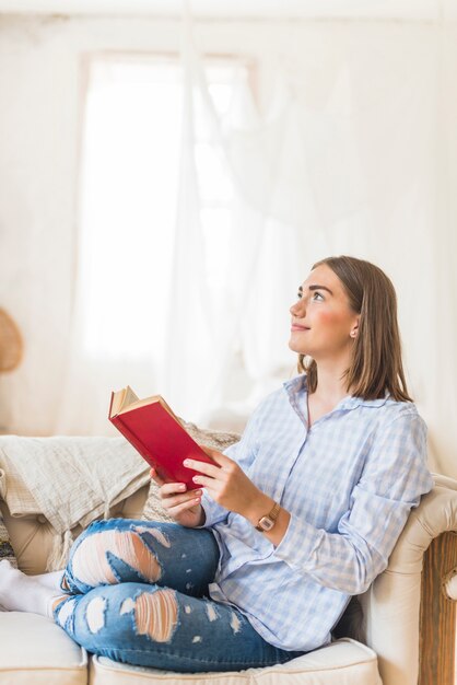 Mulher pensativa, lendo um livro no sofá