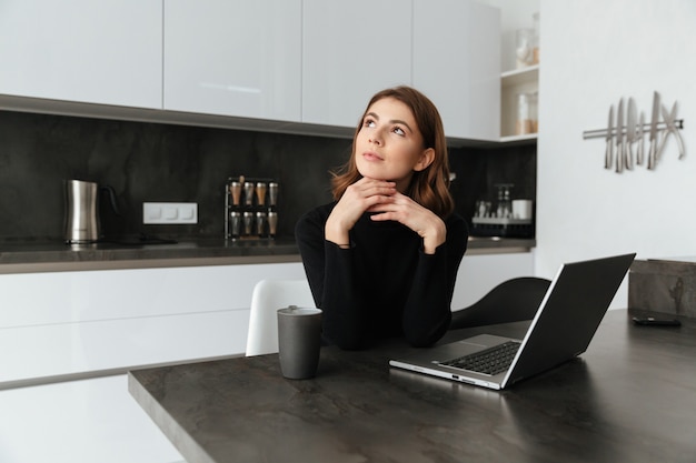 Mulher pensativa, vestida de suéter preto, sentado na cozinha