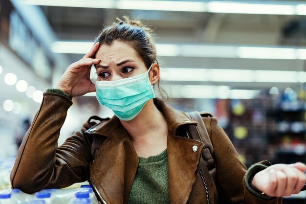 Mulher perturbada com máscara protetora pensando ao comprar no supermercado durante a epidemia de vírus