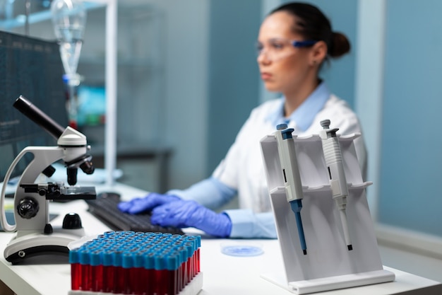 Mulher pesquisadora bióloga com jaleco branco descobrindo vacina contra vírus de digitação de perícia médica no computador. Equipamento profissional moderno em pé sobre a mesa no laboratório do hospital