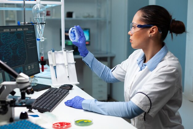 Mulher pesquisadora bióloga segurando uma placa de Petri transparente analisando a solução azul