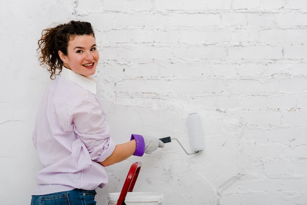 Mulher pintando parede e olhando câmera