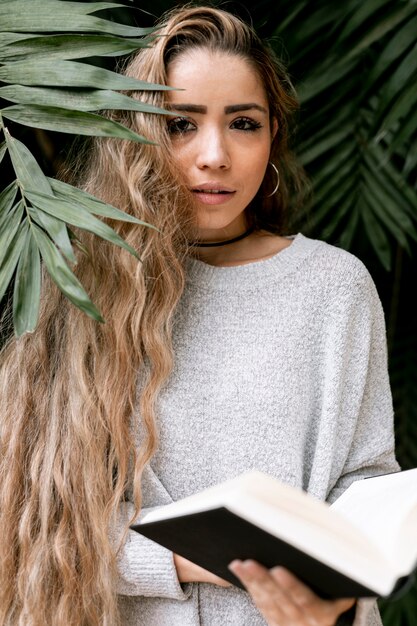 Mulher posando atrás de algumas folhas, segurando um livro