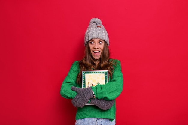 Mulher posando com um chapéu de inverno e luvas segurando um presente de natal