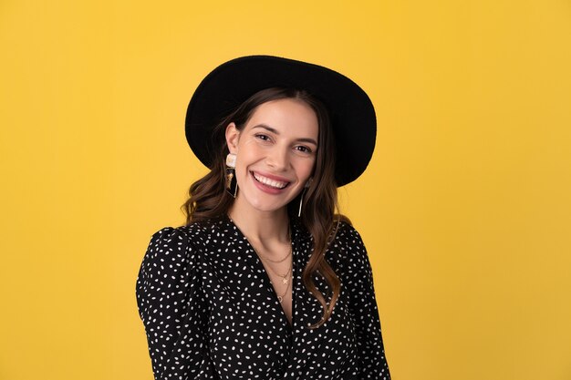 mulher posando isolada em amarelo com vestido preto pontilhado e chapéu preto elegante boho