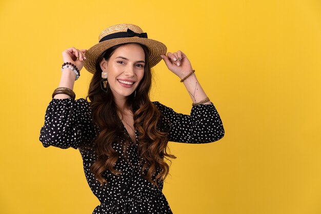 mulher posando isolada no amarelo com vestido preto pontilhado e chapéu de palha elegante boho