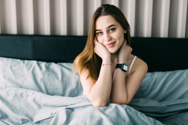 Mulher positiva com almofada sentada na cama a sorrir em casa