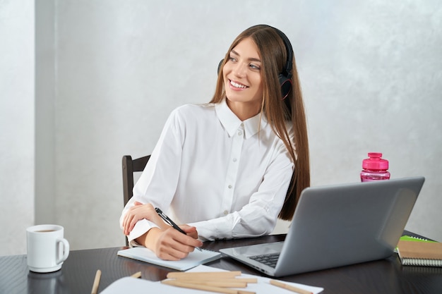 Mulher positiva em fones de ouvido, estudando no laptop