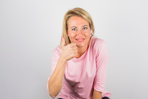 Mulher positiva sênior na blusa rosa com o polegar para cima