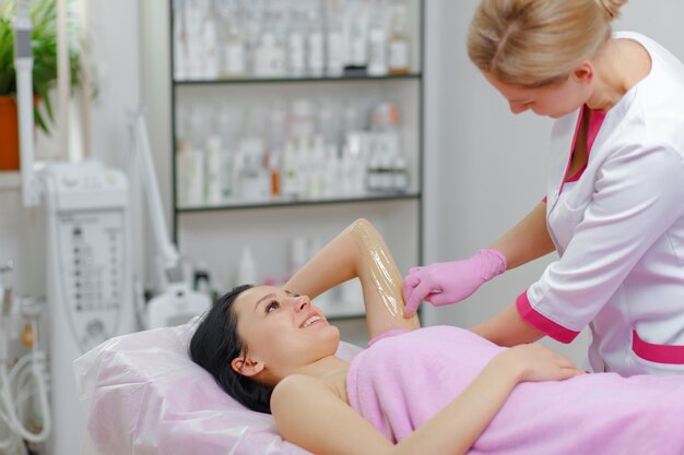 Mulher profissional fazendo cera outra mulher no braço