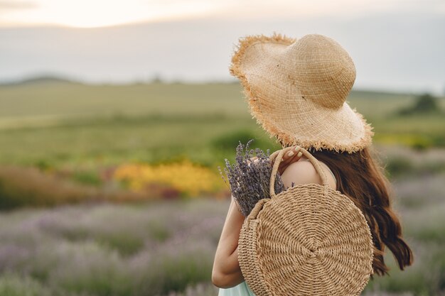 Mulher provençal relaxante no campo de lavanda. Senhora com um chapéu de palha. Menina com bolsa.