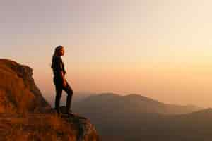 Foto grátis mulher que está em uma montanha que olha no por do sol