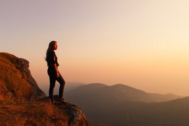 Mulher que está em uma montanha que olha no por do sol