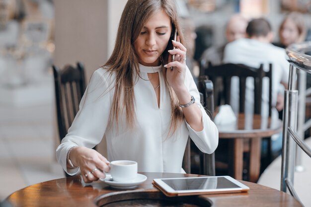 Mulher que fala no telefone e olhando para uma chávena de café