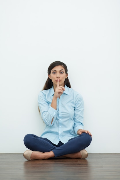 Mulher que faz o gesto do silêncio e sentado no chão