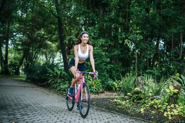 Mulher que monta uma bicicleta da estrada no parque. Retrato da mulher bonita nova na bicicleta cor-de-rosa.