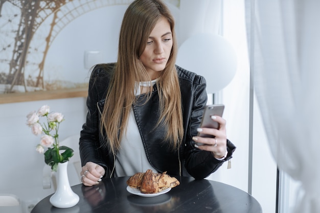 Mulher que olha seu celular com um croissant em uma placa