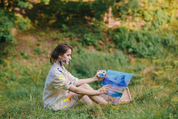 Mulher que pinta um retrato sentado na grama