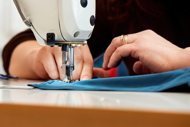 Mulher que trabalha em uma máquina de costura com tecido azul