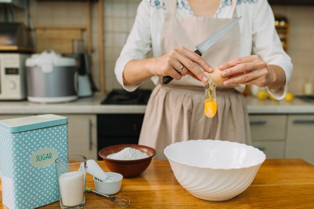 Mulher quebra ovo para fazer torta na cozinha