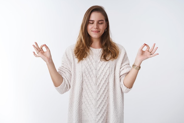 Foto grátis mulher realiza prática de ioga de respiração reunindo paciência calma sorrindo amplamente aliviado sentindo feliz relaxado em pé pose de nirvana de lótus mostrando gesto zen fechar os olhos meditando suéter solto