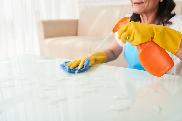 Mulher recortada de pulverização de detergente na mesa de café