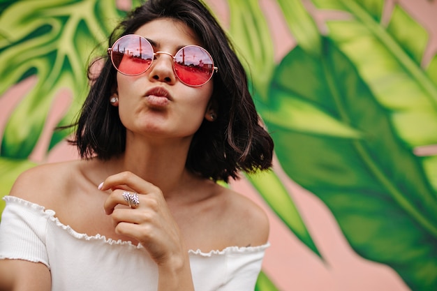 Mulher refinada em óculos de sol rosa posando com expressão facial de beijo