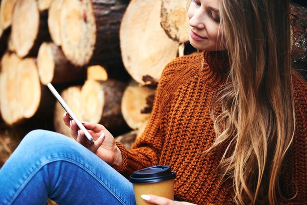 Mulher relaxando com uma xícara de café e telefone na floresta outonal