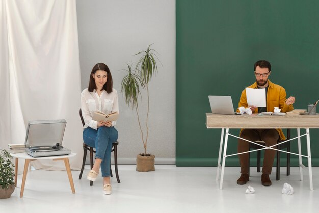 Mulher relaxando enquanto lê um livro e um homem trabalhando em um laptop