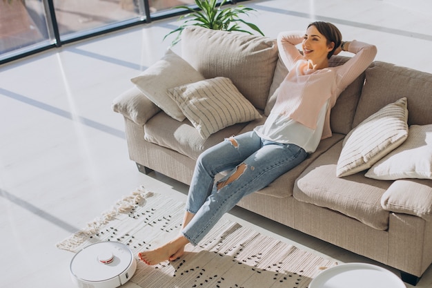 Foto grátis mulher relaxando no sofá enquanto um robô aspirador de pó faz o trabalho doméstico