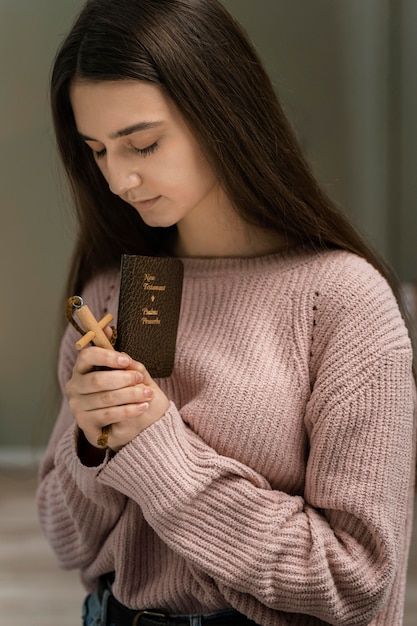 Mulher rezando com cruz de madeira e bíblia