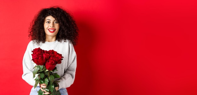 Foto grátis mulher romântica com penteado encaracolado recebe buquê de rosas vermelhas no dia dos namorados, olhando para