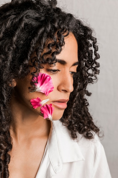 Mulher romântica étnica com pétalas de flores no rosto