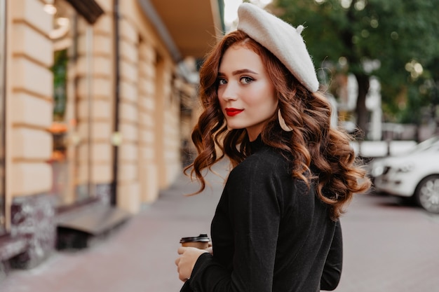 Mulher romântica ruiva na boina francesa, olhando para trás. Foto ao ar livre da adorável menina morena, aproveitando o dia de outono.